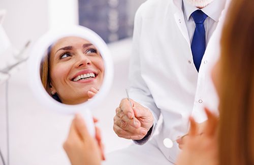 A woman admiring her treated smile with a hand mirror