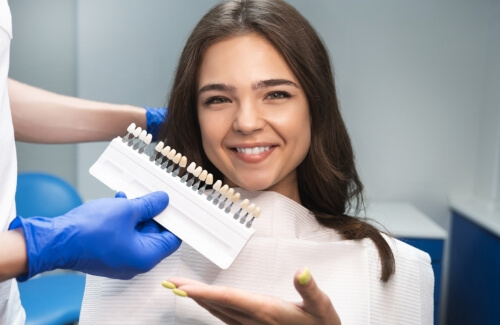 Young woman in dental chair next to dentist holding shade guide