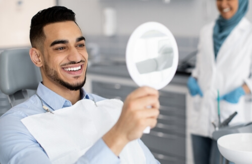 Man in dental chair looking at his smile in mirror