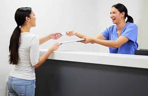 Smiling dental assistant handing patient form