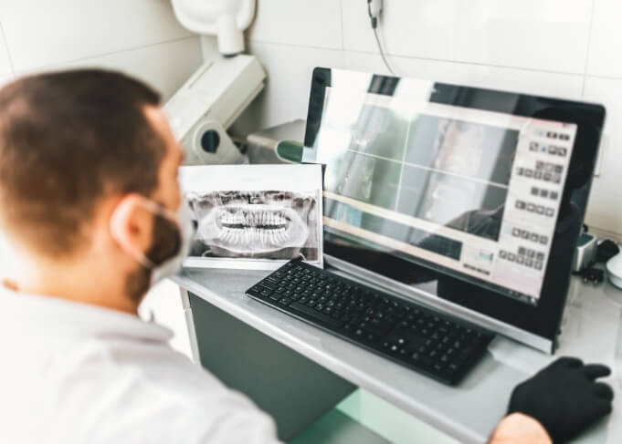 Dentist looking at computer screen with digital x rays of teeth