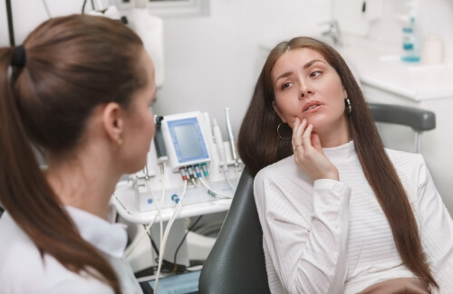 Woman holding her cheek in pain while talking to dentist