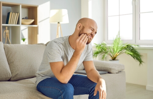 Man sitting on couch and holding his cheek in pain