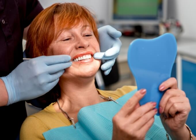 Dental patient admiring her new smile in mirror with dental implants in Grantsville