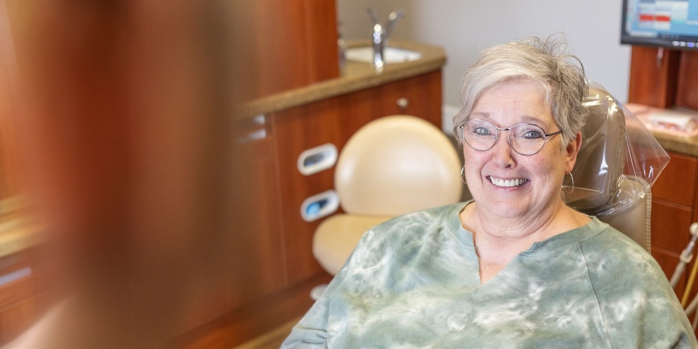 Young man in dental chair looking at his smile in mirror