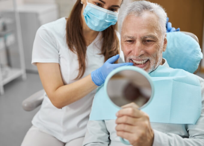 Senior dental patient admiring his smile in mirror after replacing missing teeth in Grantsville