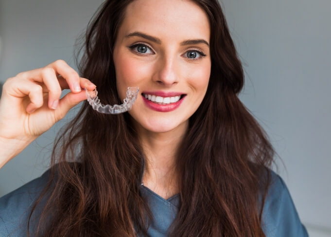 Smiling woman holding clear aligner for orthodontics in Grantsville