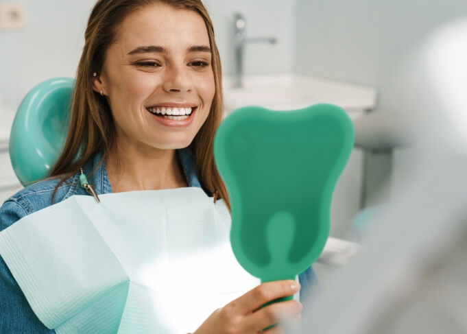 Woman admiring her smile in mirror during preventive dentistry checkup