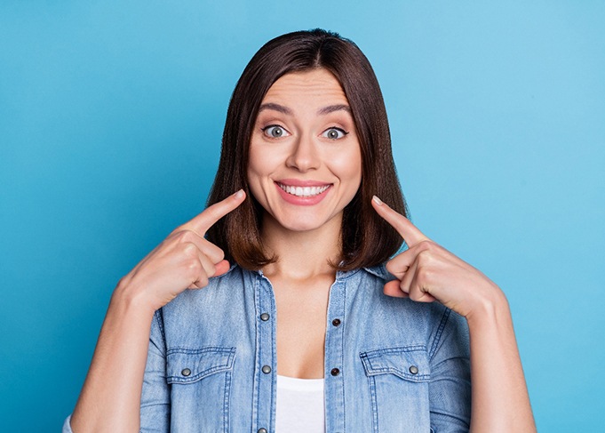 Woman pointing to her white smile with both hands with blue background
