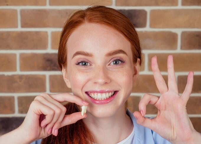 Smiling woman making okay sign while holding an extracted wisdom tooth in Grantsville